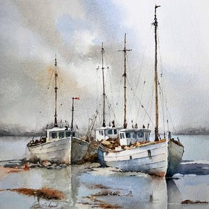 May include: A watercolor painting depicts two white fishing boats moored in shallow water. The vessels feature tall masts and weathered hulls, resting on a sandy, muddy shoreline under a soft, overcast sky. The artist's signature is visible.