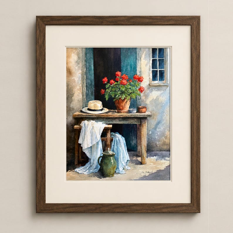 May include: A framed watercolour painting depicting a rustic wooden table and stool set against a textured wall. On the table sits a potted plant with vibrant red flowers and a straw hat. A green ceramic pitcher and draped white fabric are below.