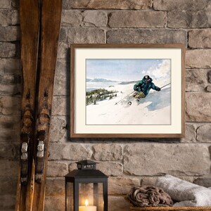 May include: A framed vintage watercolor print of a skier on a snowy slope, with a wooden frame. Two antique skis lean against a stone wall. A black lantern with a lit candle and a wicker basket with rolled blankets complete the scene.