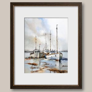 May include: A framed watercolor painting depicting three white fishing boats moored in shallow water. The scene features tall masts, soft blue and grey sky tones, and brown reflections on the water surface, all enclosed in a dark brown frame.
