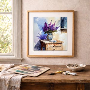 May include: A framed watercolor painting depicts a still life with a vase of purple flowers on a small wooden table. The painting is in a light-colored wooden frame. A palette, paint tubes, and a bowl are on a wooden table in the foreground.
