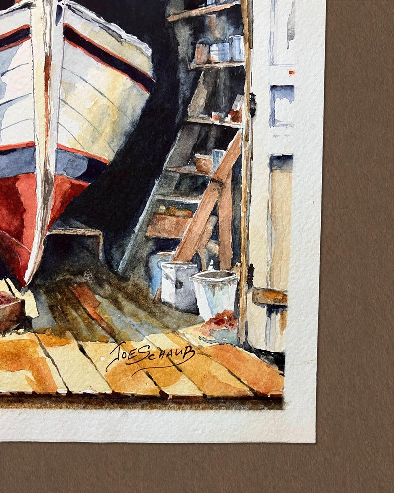 May include: A watercolor painting depicting a boat hull in a workshop with wooden floorboards, shelves holding various containers, and a white door frame. The artist's signature, Joe Schaub, is visible in black ink on the lower wooden floor area.