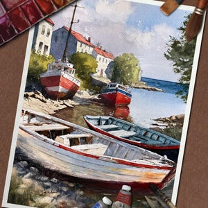 May include: Watercolor painting of boats on a shore with buildings in the background. The boats are red, white, and blue. The painting is on a white paper with paint tubes and brushes around it.