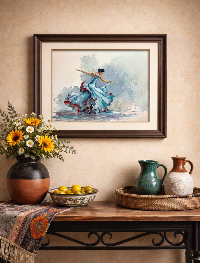May include: A framed watercolor painting of a flamenco dancer in a flowing blue dress with red accents. The artwork hangs above a table with a vase of sunflowers, a bowl of lemons, and decorative pitchers.