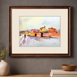 May include: Watercolour painting depicting a village scene with vibrant buildings and a person in a red coat walking along a path. The artwork is framed in a dark brown wooden frame with a white mount.