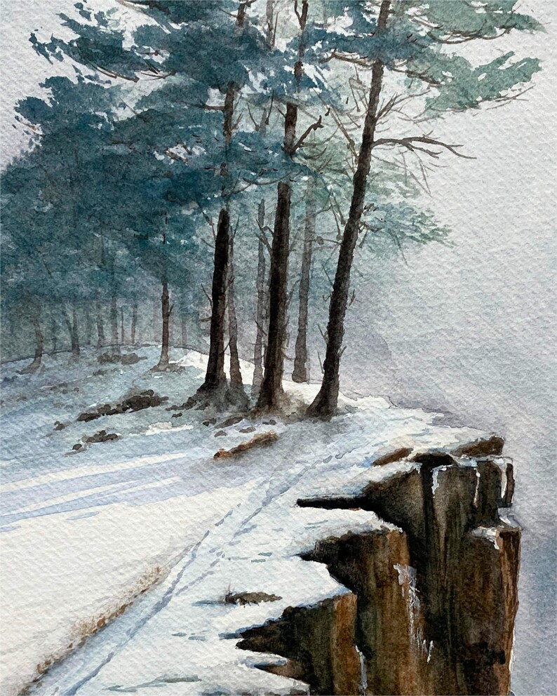 K&ouml;nnte beinhalten: Aquarellmalerei einer verschneiten Waldszene. Hohe, schlanke B&auml;ume mit blau-gr&uuml;nem Laub stehen an einer schneebedeckten Klippe. Das Gem&auml;lde f&auml;ngt das weiche Licht und die Atmosph&auml;re einer Winterlandschaft ein.