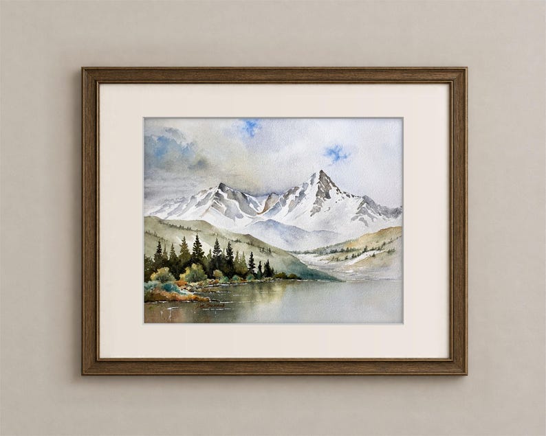 May include: A framed watercolor painting depicting a landscape with snow-capped mountain peaks, a calm lake in the foreground, and a dense forest of dark green pine trees along the shoreline under a cloudy sky with patches of blue.