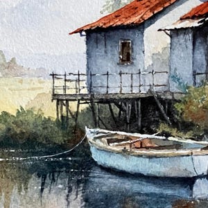 May include: Watercolor painting of a coastal scene featuring two weathered, light blue buildings with red roofs. A small white boat floats in the water, tied to the shore. The artwork depicts a serene landscape with muted colors and a sense of tranquility.