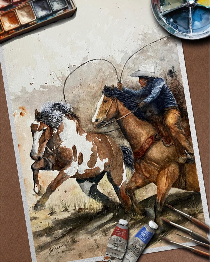 May include: Watercolor painting of a cowboy on horseback roping a horse. The painting features a brown and white horse running alongside a brown horse with a rider. Paint tubes and brushes are in the foreground.