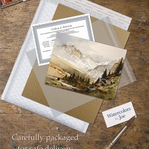 May include: A watercolor landscape painting of mountains and pine trees, a Certificate of Authenticity, a white bubble mailer, a brown cardboard insert, a business card reading Watercolors By Joe, and a wooden paintbrush on a wooden surface.