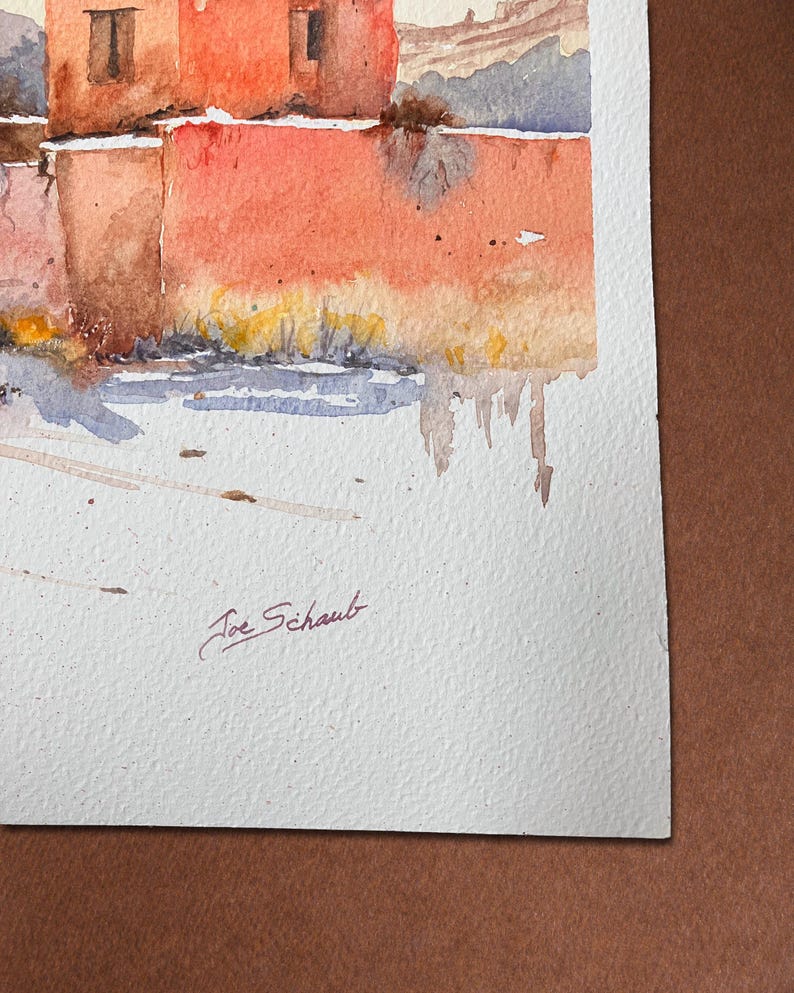 May include: Watercolour painting depicting a building with red-orange walls and small windows. The artwork uses a muted colour palette with shades of red, brown, and blue. The artist's signature, "Joe Schaub," is visible in the lower left corner.