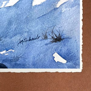 May include: Watercolor painting of a mountain landscape in shades of blue and white. The artwork features a signature in the lower left corner and a few tufts of grass. The painting is mounted on a white paper with a torn edge.
