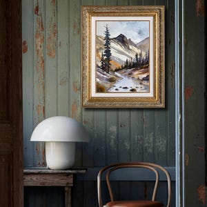 May include: A framed landscape painting with a gold ornate frame hangs on a distressed green wall. The painting depicts a mountain scene with a river and trees. A white mushroom-shaped lamp sits on a wooden table below the painting.
