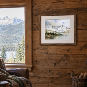 May include: A framed watercolor painting depicting a snow-capped mountain range above a calm lake and a line of dark green pine trees. The artwork is displayed in a light-colored mat and a brown wooden frame, hanging on a rustic wood-paneled wall.