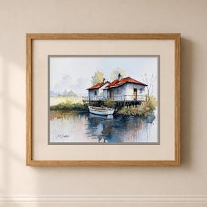 May include: Watercolor painting of two small white houses with red roofs on stilts over water. A small white boat floats nearby. The artwork is framed in a light brown wooden frame.