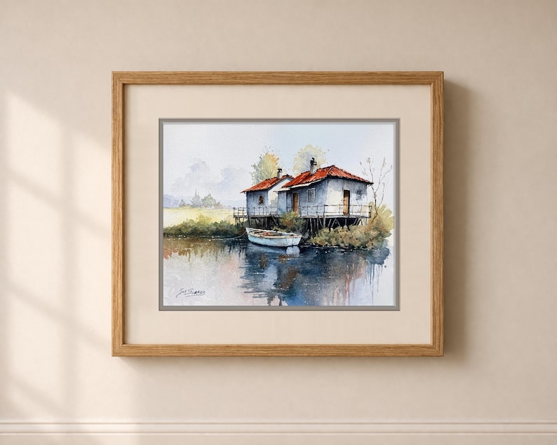May include: Watercolor painting of two small white houses with red roofs on stilts over water. A small white boat floats nearby. The artwork is framed in a light brown wooden frame.