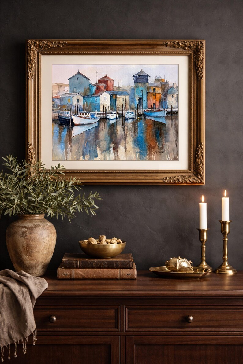 May include: A framed watercolor painting of a harbor scene with boats and buildings in shades of blue, orange, and white. The painting is displayed above a wooden cabinet with decorative items, including a vase, bowl, books, and candlesticks.