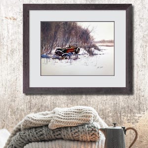 May include: A framed watercolour painting shows a vintage red truck in a snowy scene. The truck is partly covered in snow, set against bare trees and a muted sky. The dark brown frame surrounds the painting, which is displayed above a stack of grey blankets.