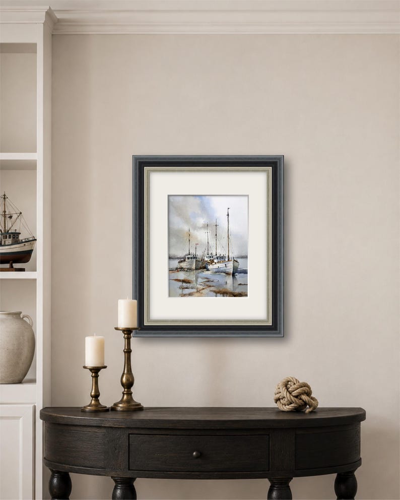 May include: A framed watercolor painting depicting several white fishing boats docked in shallow water under a cloudy sky. The artwork is enclosed in a dark gray frame with a white mat, showcasing a maritime scene with reflections on the water surface.