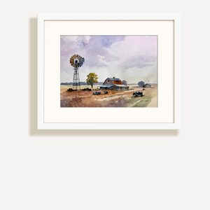 May include: Watercolor painting of a rural landscape featuring a windmill, barn, and fields under a cloudy sky. The artwork is framed in a white mat and frame, showcasing a serene farm scene with muted colors.