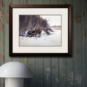 May include: A framed watercolour painting shows a vintage car in a snowy scene. The car, with a red body and black details, is partly covered in snow. The artwork is set against bare trees and a muted, wintery sky. The frame is dark brown.