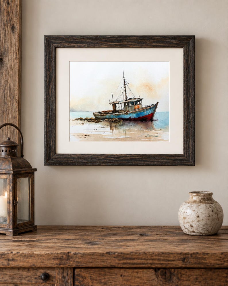 May include: A framed watercolor painting depicting a weathered blue and red fishing boat resting on a sandy shore. The artwork features soft, muted tones of beige and light blue in the background, with a dark brown textured wooden frame.