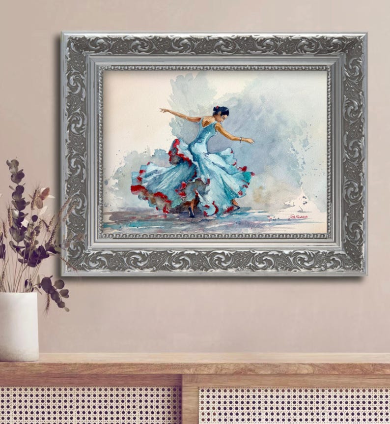 May include: Watercolor painting of a dancer in a flowing blue dress with red accents, framed in a silver ornate frame. The artwork captures the dancer mid-motion, with arms outstretched. The background features soft, watercolor washes.