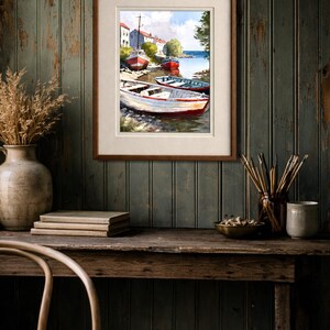 May include: A framed watercolor painting depicts a coastal scene with several small boats docked near a shore. The boats are painted in shades of red, white, and blue. The artwork is displayed on a wooden desk with other decorative items.