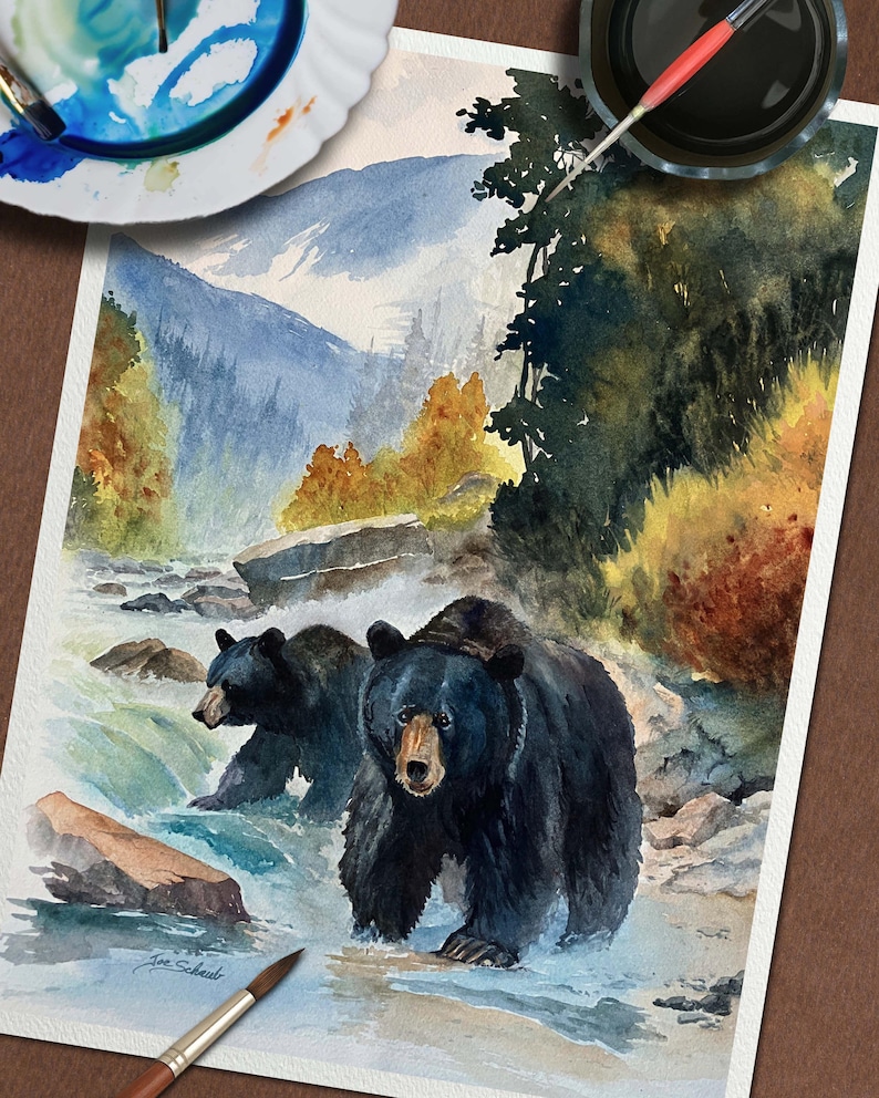 以下が含まれることがあります： 川の中にいる2匹の黒い熊を描いた水彩画。背景には山々が描かれています。青、緑、茶色を基調とした作品で、筆とパレットが描かれています。Joe Schueltのサイン入りです。
