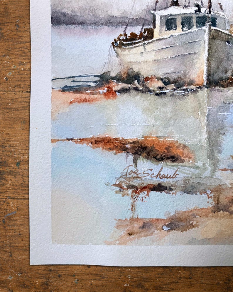 May include: A watercolor painting depicting a white fishing boat docked near a shoreline with muted gray, blue, and earthy brown tones. The artwork features a soft, atmospheric reflection on the water and includes the signature Joe Schaub in ink.