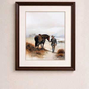 May include: Watercolor painting in a dark brown frame. The artwork depicts a cowboy walking alongside a horse on a dirt path. The horse is saddled and the cowboy is wearing a hat and jeans. The background shows a hazy landscape.