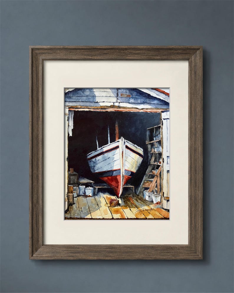 May include: A framed watercolor painting depicting a white boat with a red hull resting inside a dark wooden boathouse. The scene features a wooden floor, storage shelves, and a signature in the bottom right corner. The frame is dark brown wood.