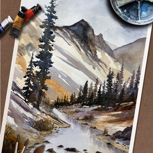May include: Watercolor painting of a mountain landscape with a river. The artwork features a detailed depiction of a mountain range, a flowing river, and evergreen trees. Paint tubes and brushes are visible, suggesting the painting process.