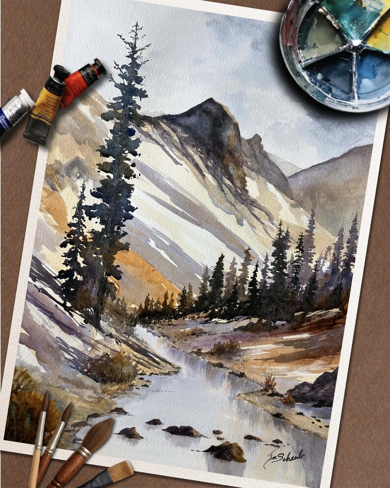 May include: Watercolor painting of a mountain landscape with a river. The artwork features a detailed depiction of a mountain range, a flowing river, and evergreen trees. Paint tubes and brushes are visible, suggesting the painting process.