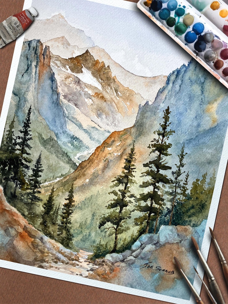 May include: Watercolor painting of a mountain landscape with evergreen trees in the foreground. The artwork features shades of blue, brown, and green, with a palette of watercolor paints and brushes visible. The artist's signature is in the lower right corner.