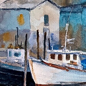 May include: Watercolor painting of a harbor scene with two white boats docked near buildings. The boats have brown accents and are reflected in the water. The buildings are light blue and beige with dark roofs.