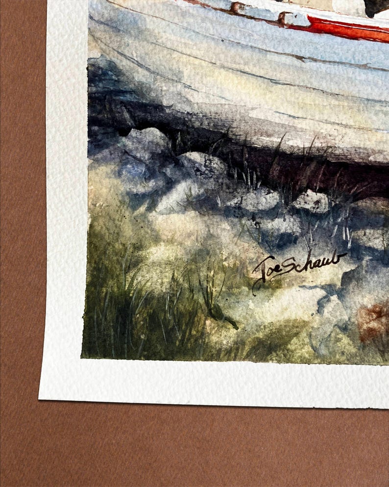 May include: Watercolor painting of a boat on a rocky shore. The boat has a red stripe along the top edge. The artist's signature, "Joe Schaub", is visible in the lower right corner. The painting is on textured paper.