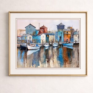 May include: Watercolor painting of a harbor scene with boats docked near colorful buildings. The artwork features a gold frame and a serene reflection of the buildings and boats in the water, with a signature in the bottom right corner.