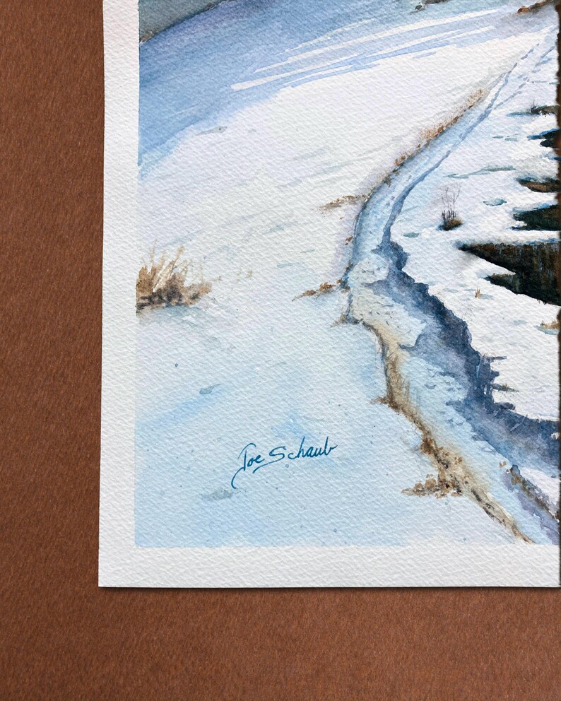 K&ouml;nnte beinhalten: Aquarellmalerei einer verschneiten Landschaft mit einem gewundenen Pfad. Das Kunstwerk zeigt Blau- und Wei&szlig;t&ouml;ne, die eine Winterszene darstellen. Unten rechts signiert mit "Joe Schaub".
