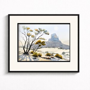 May include: Watercolor landscape art print featuring a desert scene with a prominent mesa in the background. A tree with yellow and green foliage is in the foreground, casting long shadows. The artwork is framed in a black frame with a white mat.