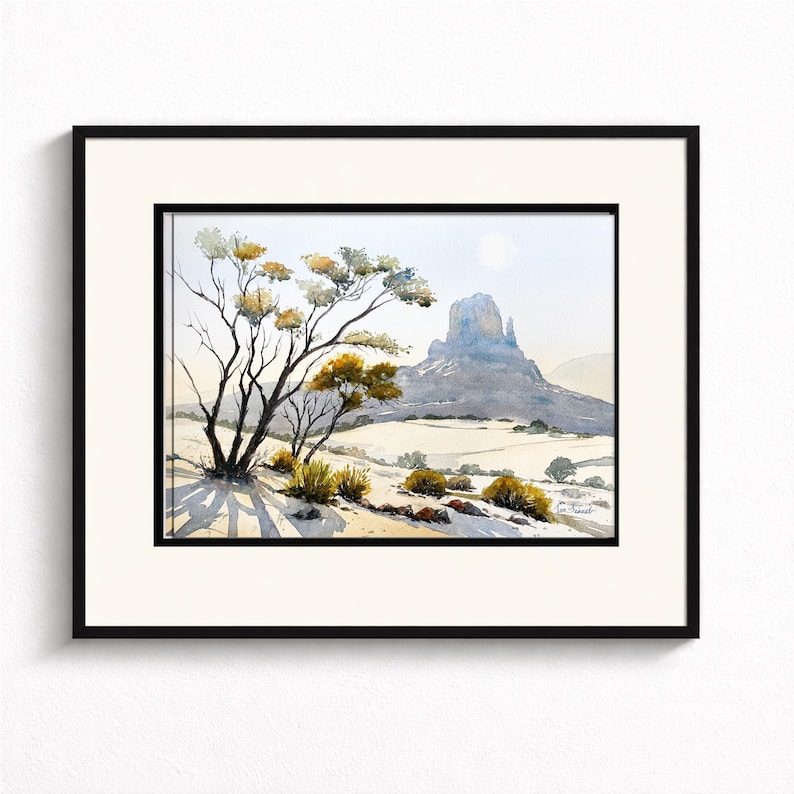 May include: Watercolor landscape art print featuring a desert scene with a prominent mesa in the background. A tree with yellow and green foliage is in the foreground, casting long shadows. The artwork is framed in a black frame with a white mat.