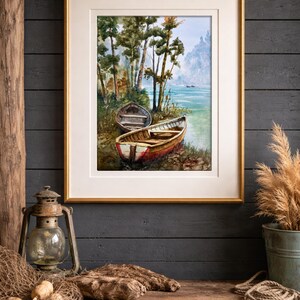 Op de afbeelding: Een ingelijste aquarel van twee boten aan een oever met bomen. De schildering zit in een gouden lijst en wordt tentoongesteld op een rustiek houten oppervlak. Een vintage lantaarn en visnet staan op de voorgrond.