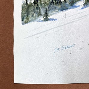 May include: Watercolor painting of a snow-covered mountain slope with evergreen trees. The artwork features a serene winter landscape with long shadows cast across the snow. The artist's signature, "Joe Schaub," is visible in the lower right corner.
