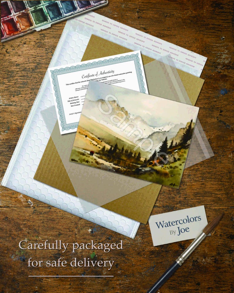 Pu&ograve; includere: Un dipinto paesaggistico ad acquerello con montagne e pini, un certificato di autenticit&agrave;, un supporto in cartone marrone, una busta imbottita bianca, un biglietto da visita con scritto Watercolors By Joe e un pennello con manico scuro e setole marroni.