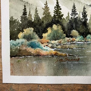 May include: A watercolor painting depicting a landscape with a calm body of water in the foreground, a shoreline with green and brown bushes, and a dense forest of dark green pine trees. In the background, soft, muted hills rise under a pale sky.