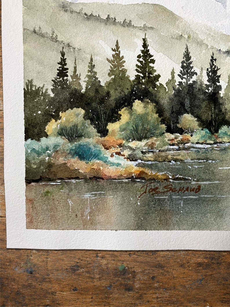 May include: A watercolor painting depicting a landscape with a calm body of water in the foreground, a shoreline with green and brown bushes, and a dense forest of dark green pine trees. In the background, soft, muted hills rise under a pale sky.