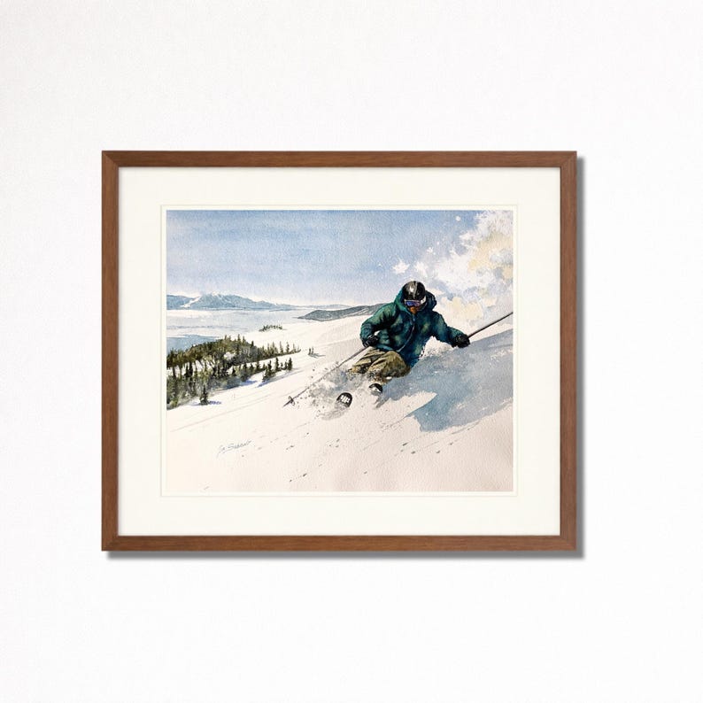 May include: Watercolor print of a skier carving down a snowy mountain slope. The skier wears a green jacket and black helmet. The artwork is framed in a brown wooden frame with a white matting, and depicts a winter landscape with trees and a lake.