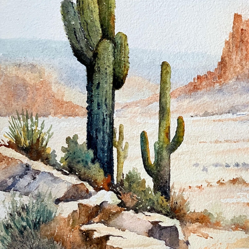 May include: A watercolor painting of a desert landscape featuring two tall green saguaro cacti in the foreground. The scene includes rocky terrain, sparse desert vegetation, and distant orange-toned rock formations under a pale sky.