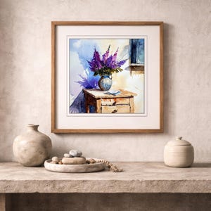 May include: Watercolor painting of a vase of purple flowers on a wooden table, framed in a light brown wooden frame. The table has two drawers and a small book. The background features a window and a wall with soft blue and white hues.