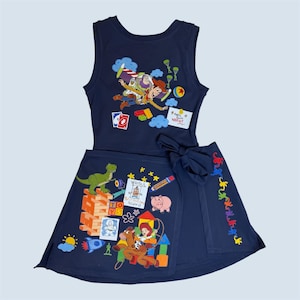 May include: Navy blue two-piece outfit featuring characters from the animated film Toy Story. The top is a sleeveless tank with Buzz Lightyear and Woody. The skirt has a wrap design with a bow and additional Toy Story graphics.